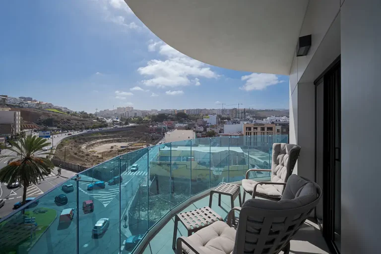 Terraza con sillones y barandilla de vidrio, vista de la ciudad y el cielo.