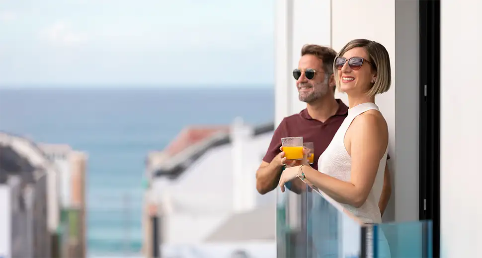 Pareja sonriente con bebidas en un balc&oacute;n frente al mar