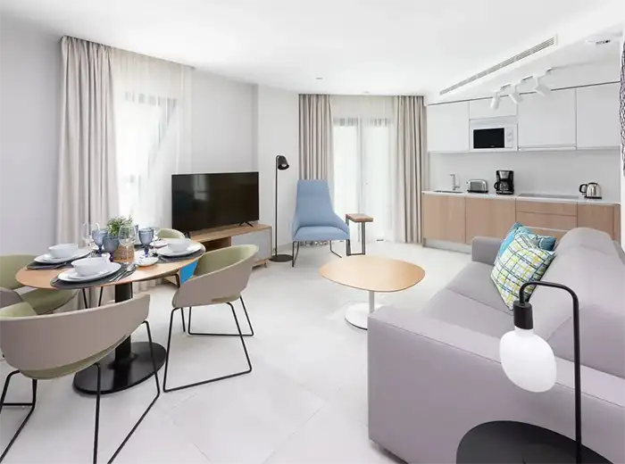 Sala moderna con sof&aacute;, mesa, cocina integrada y comedor con sillas.