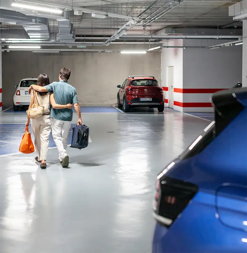 Personas caminando por garaje con coches estacionados y se&ntilde;ales rojas/blancas.