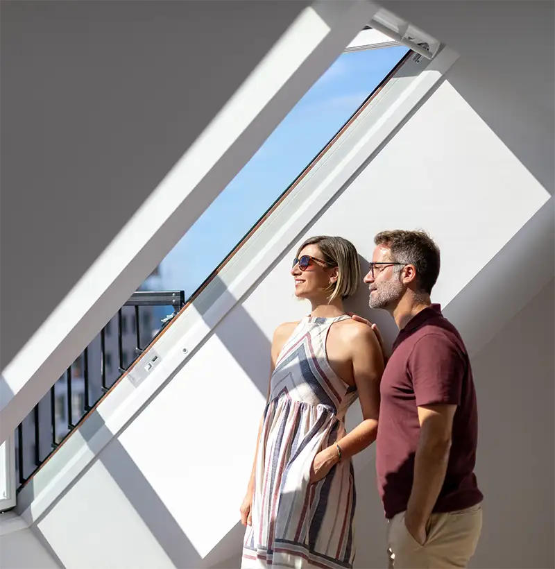 Pareja joven en un edificio moderno, mirando por una ventana abierta.