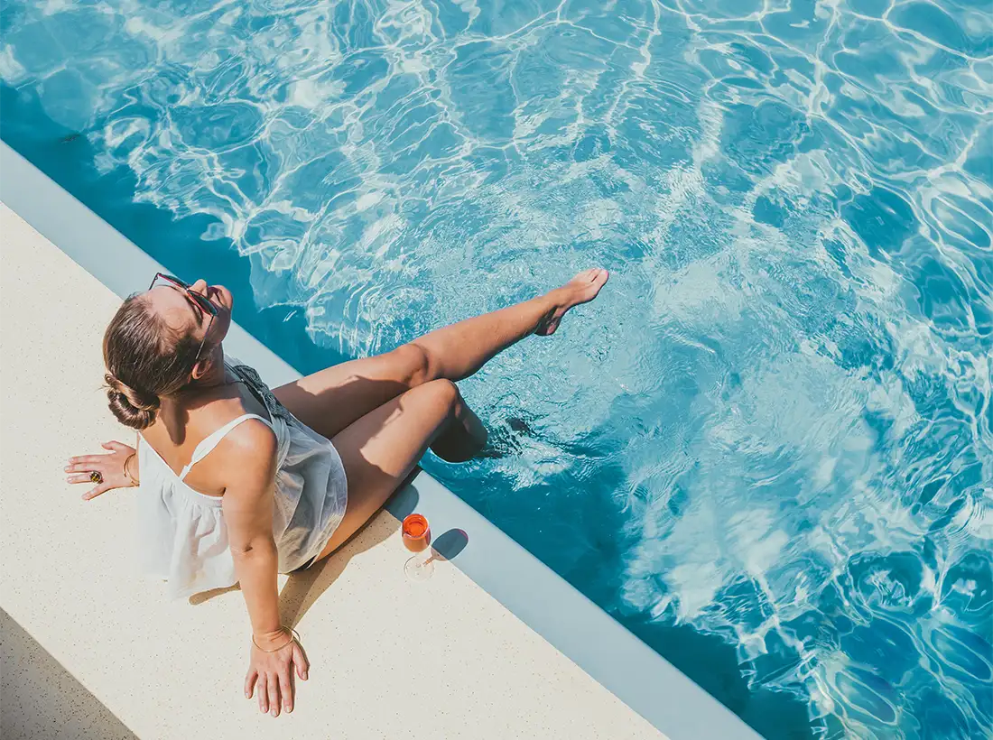 Mujer recostada en el borde de una piscina azul, con balde naranja.