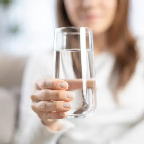 Mujer sostiene un vaso de agua frente a la c&aacute;mara.
