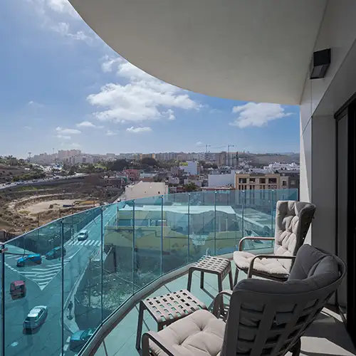 Balc&oacute;n con sillones y vista urbana desde un edificio, con cielo nublado