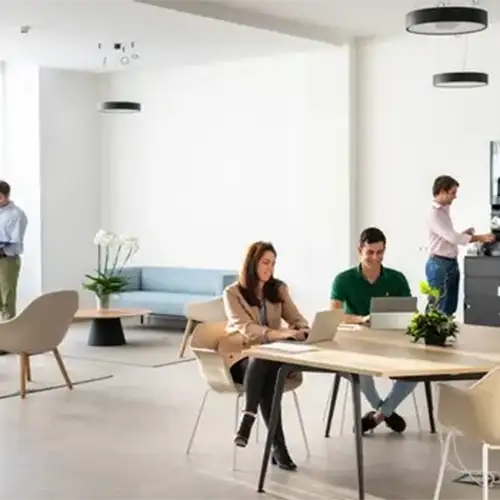 Oficina moderna con tres personas trabajando en una mesa compartida