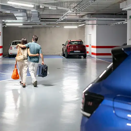 Personas en un garaje subterr&aacute;neo con coches estacionados y luces del techo.