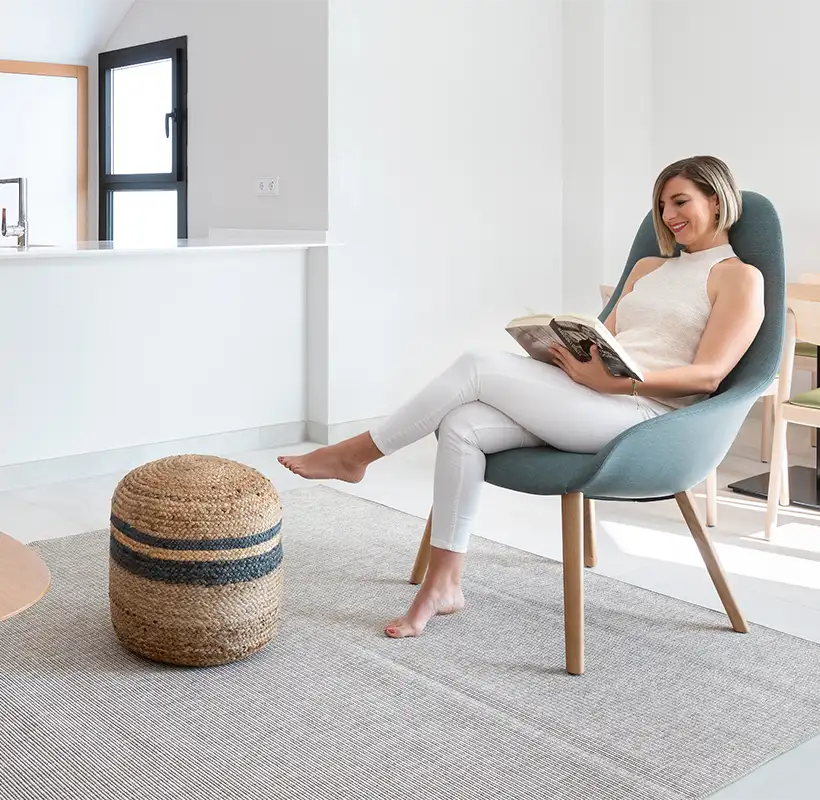 Mujer leyendo una revista sentada en un sill&oacute;n azul en un interior luminoso.