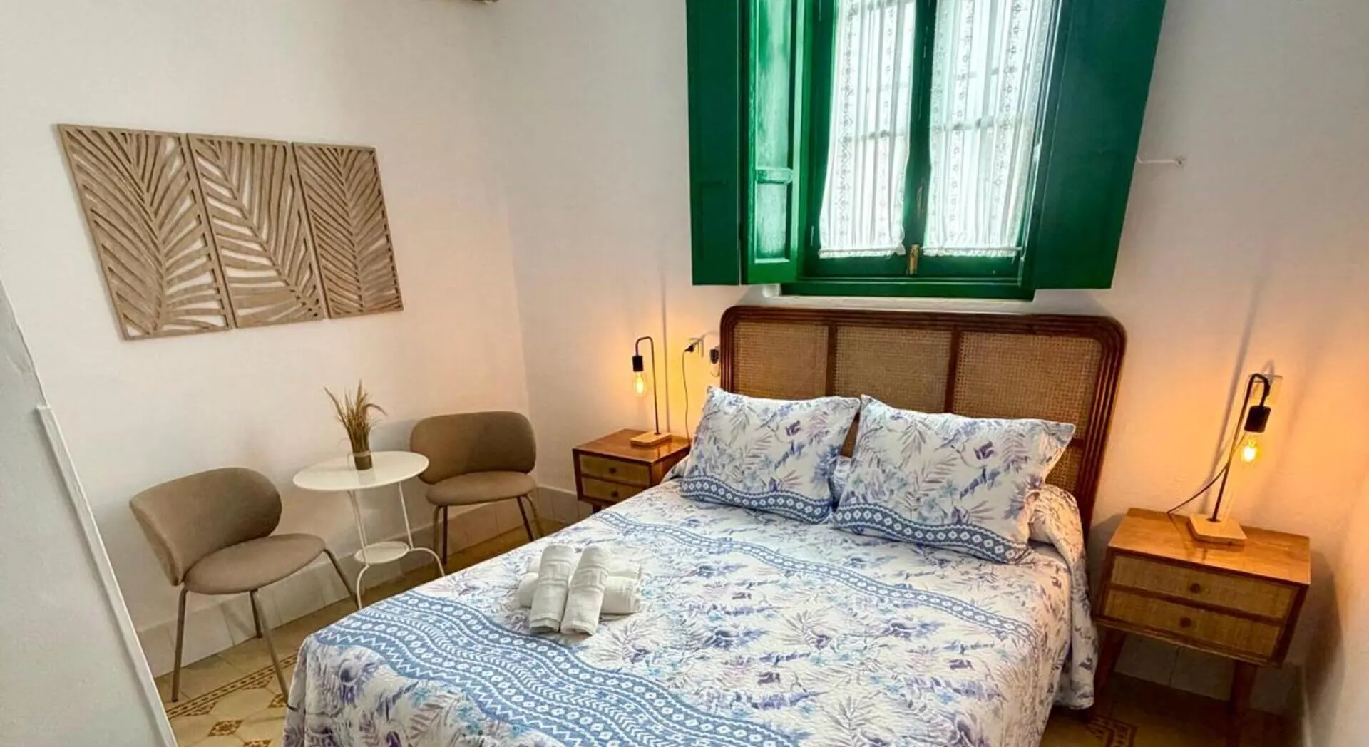 Dormitorio con cama, almohadas azules, sill&oacute;n y ventana verde
