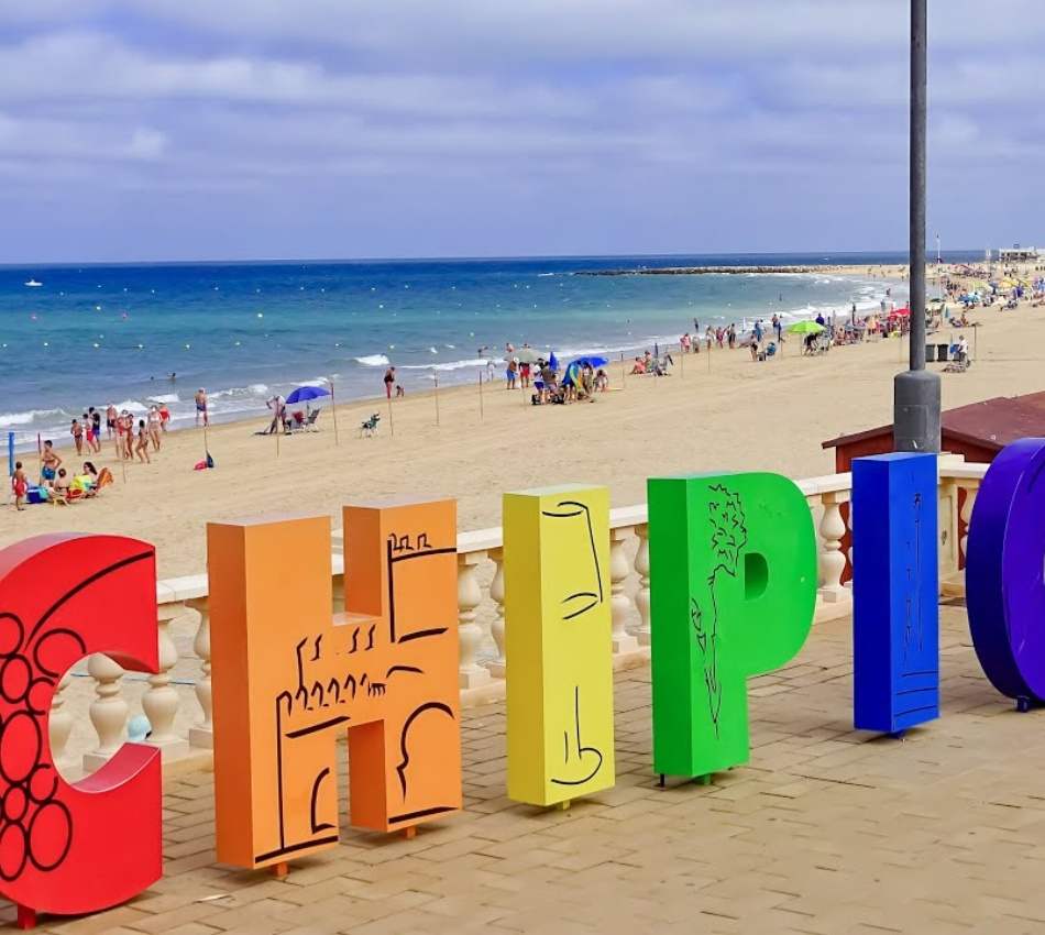 Cartas de letras de colores en la costa, con playa y gente al fondo
