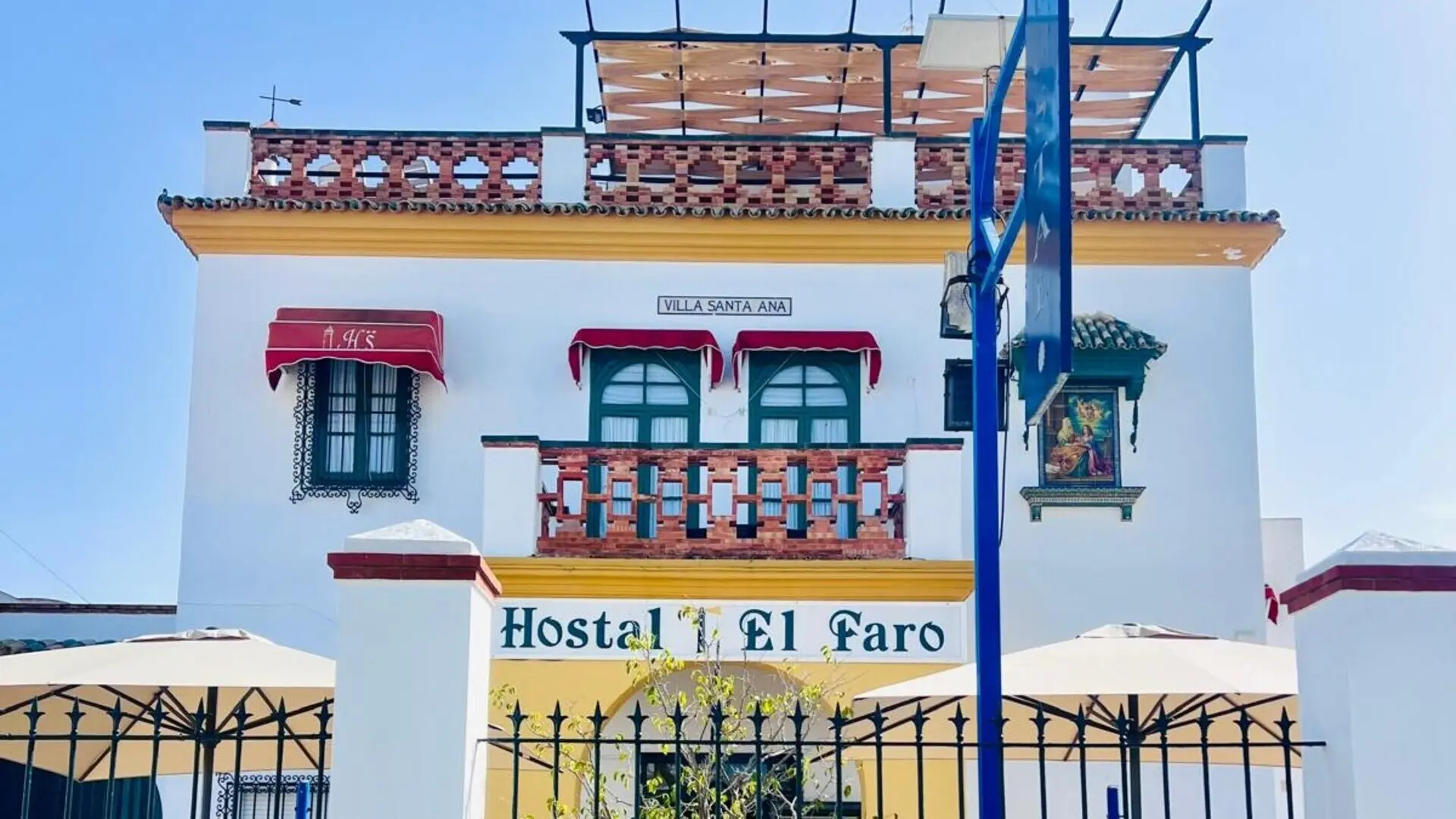 Fachada de &ldquo;Hostal El Faro&rdquo; con gr&uacute;a azul y ventana en el piso superior