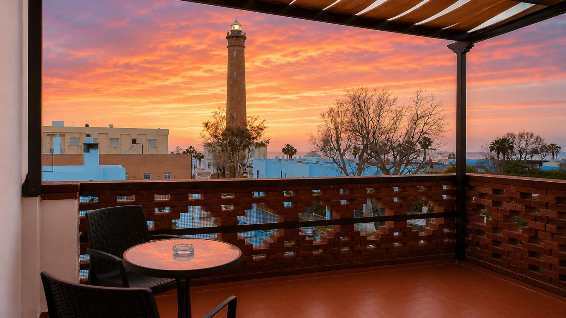 Terraza con faro en el horizonte y atardecer anaranjado desde el balc&oacute;n