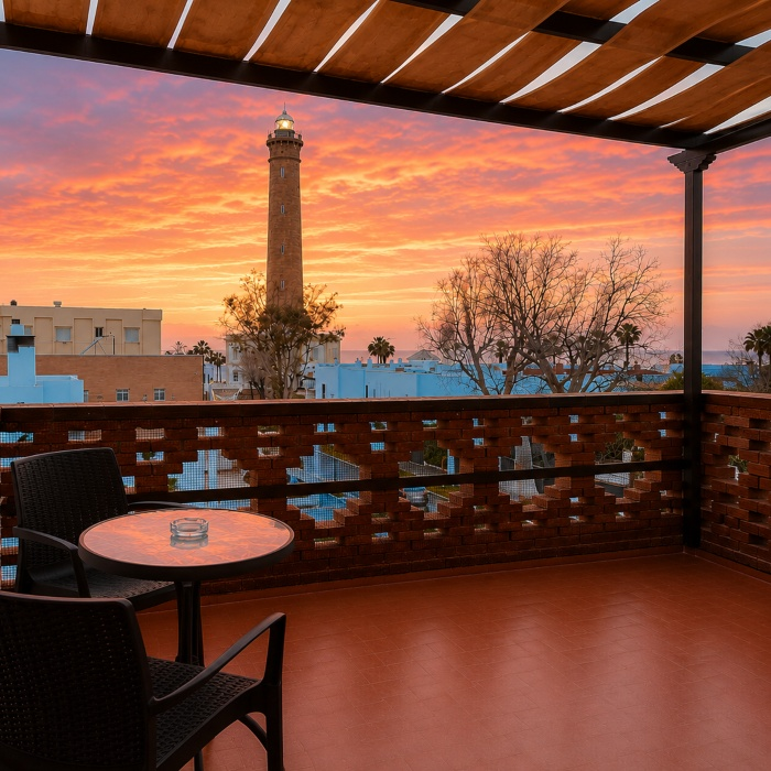 Terraza con mesa y faro al atardecer, cielo rosado y vistas a la ciudad
