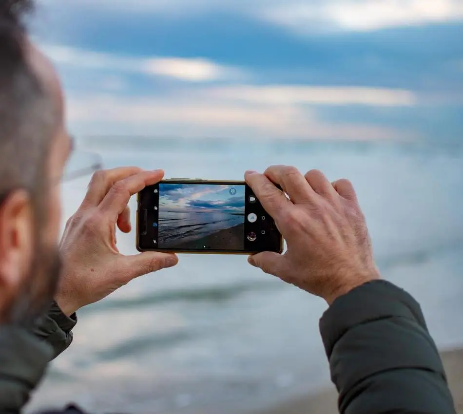 Persona sostiene un tel&eacute;fono y fotograf&iacute;a el mar con la pantalla en uso