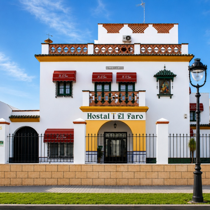 Fachada del Hostal El Faro, con balcones y letrero, cielo azul.