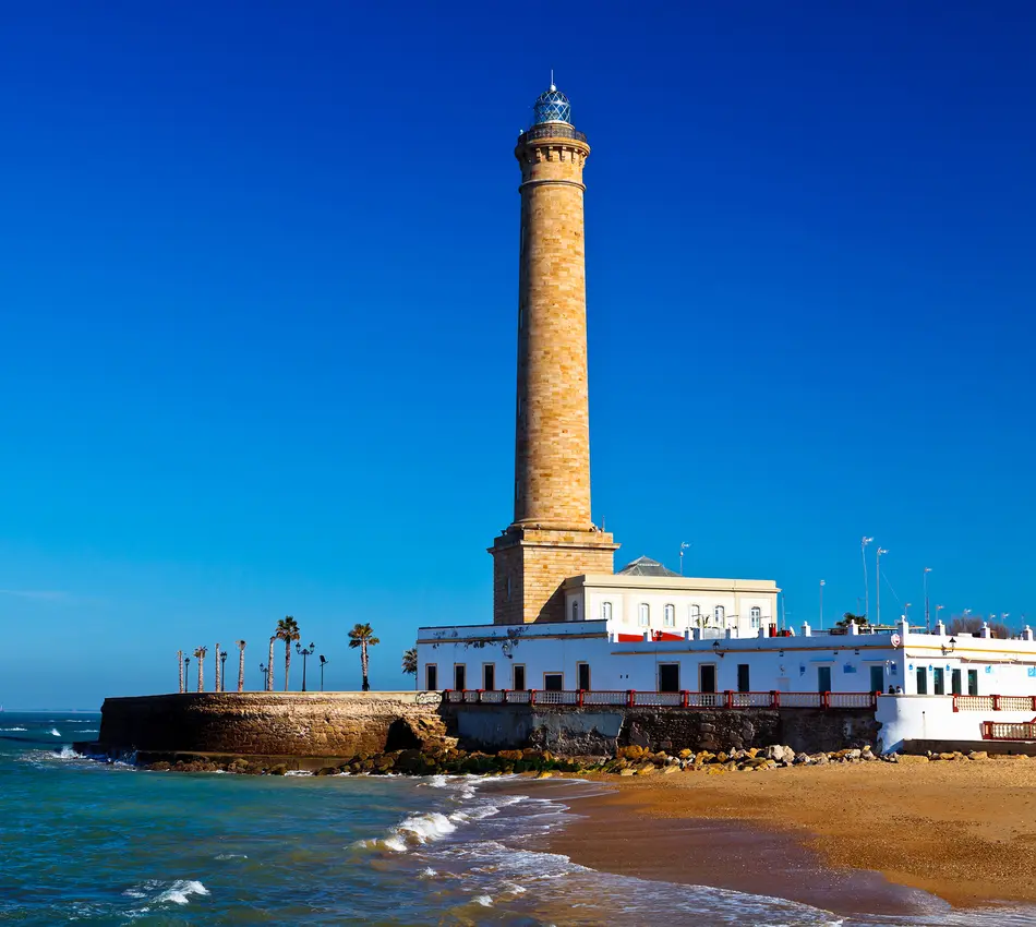 Faro alto junto al mar, con cielo azul y playa al frente