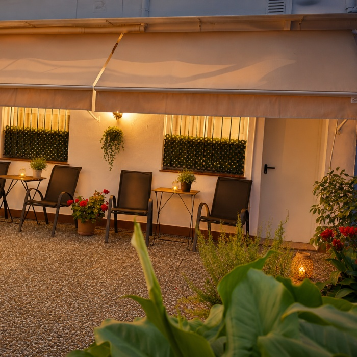 Patio con sillas, flores y luces c&aacute;lidas bajo un toldo beige