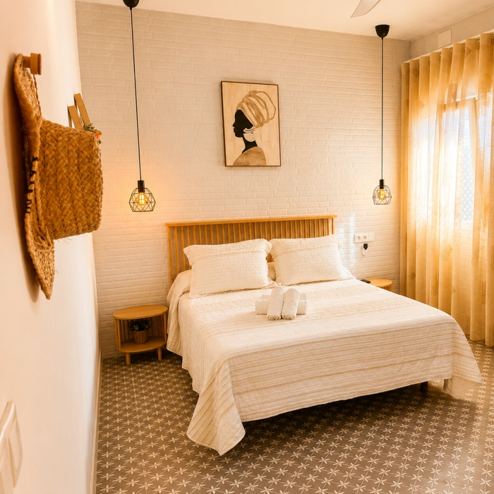 Dormitorio con cama doble blanca, l&aacute;mparas colgantes y paredes blancas