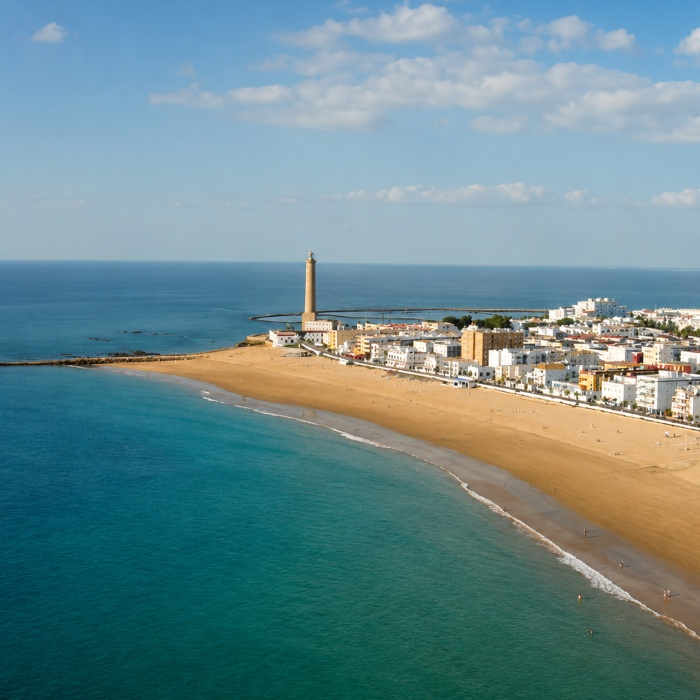 Vista a&eacute;rea de una playa con faro y un pueblo costero frente al mar