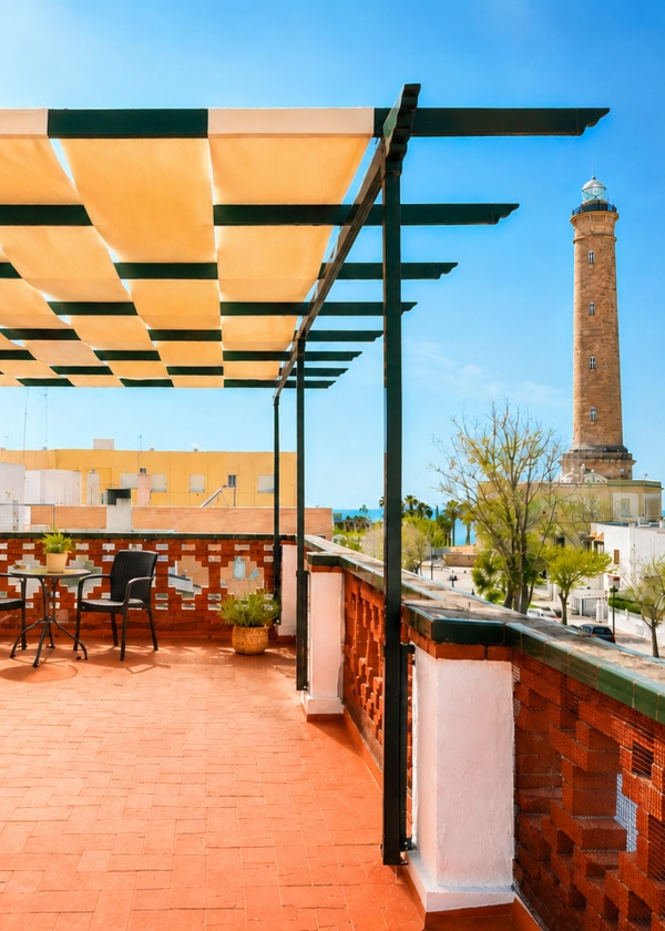 Terraza con toldo y silla; faro alto al fondo bajo cielo azul