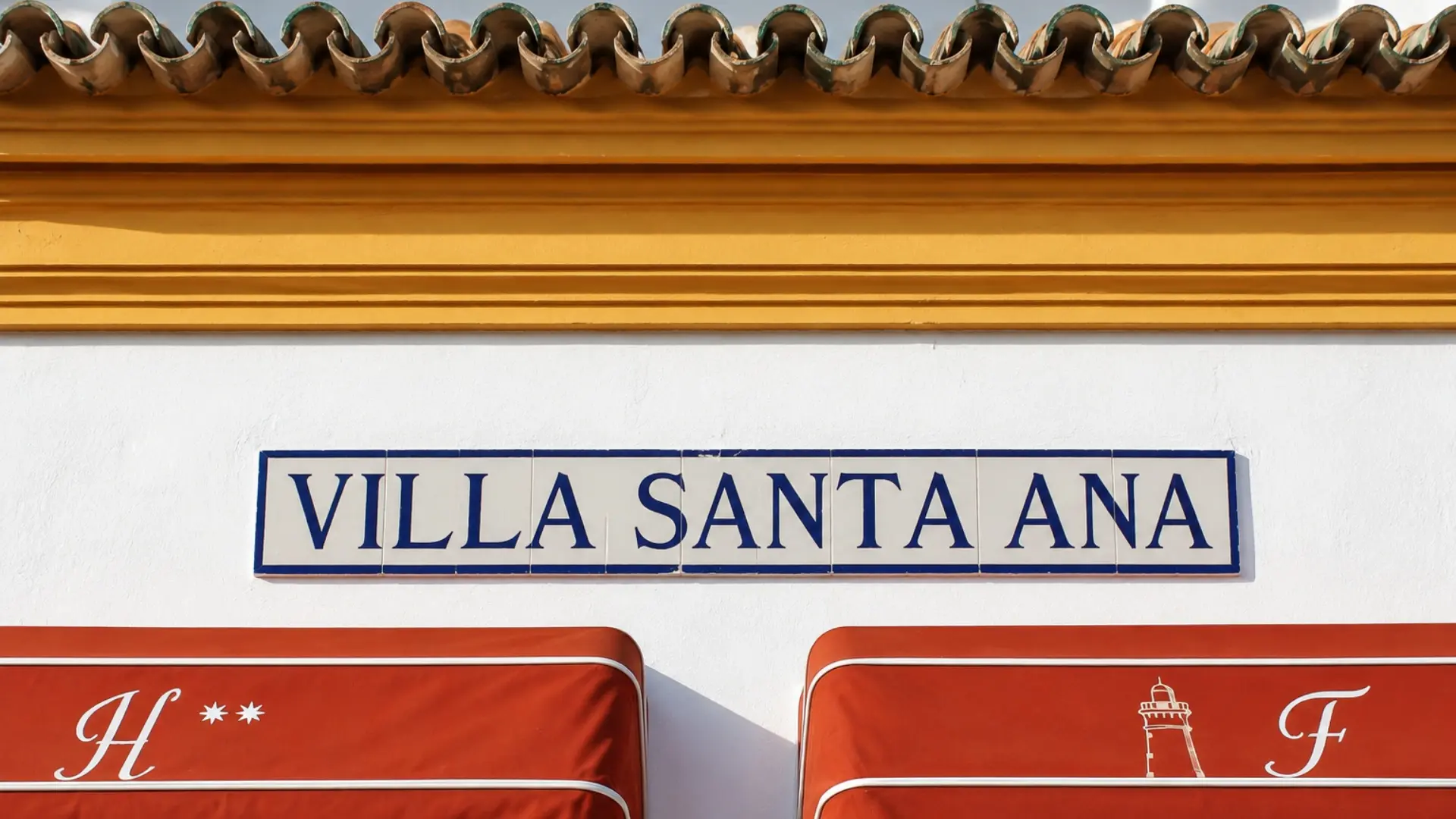 Placa &ldquo;VILLA SANTA ANA&rdquo; en pared blanca, con asientos naranjas abajo