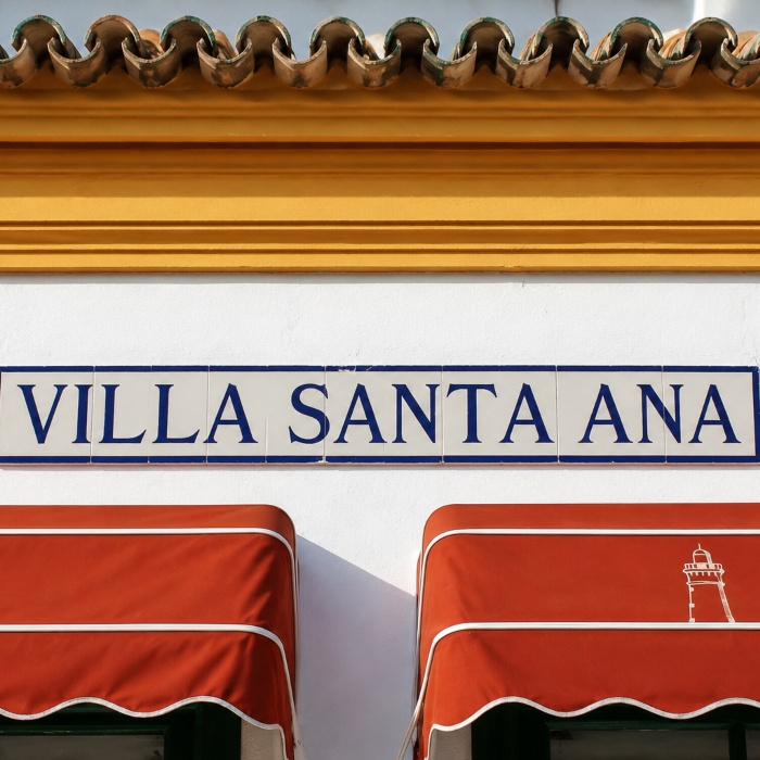 Cartel &ldquo;VILLA SANTA ANA&rdquo; sobre toldos rojos con faro dibujado.