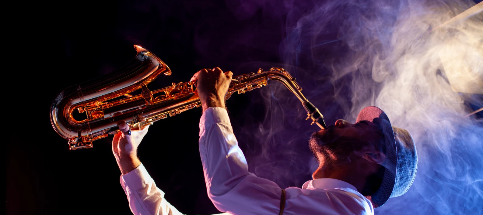 Trompetista con saxof&oacute;n entre humo, luz c&aacute;lida y fondo oscuro.