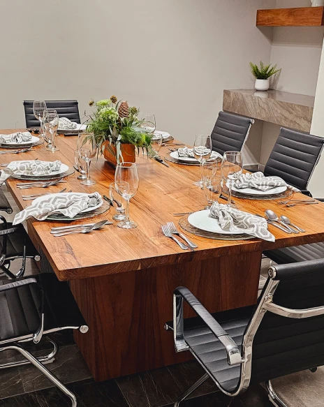 Mesa de comedor con cubiertos y copas, arreglos verdes y plantas decorativas