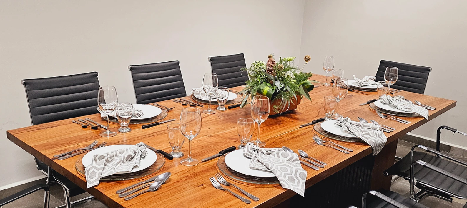Mesa de comedor con vajilla, copas y manteles blancos sobre madera.