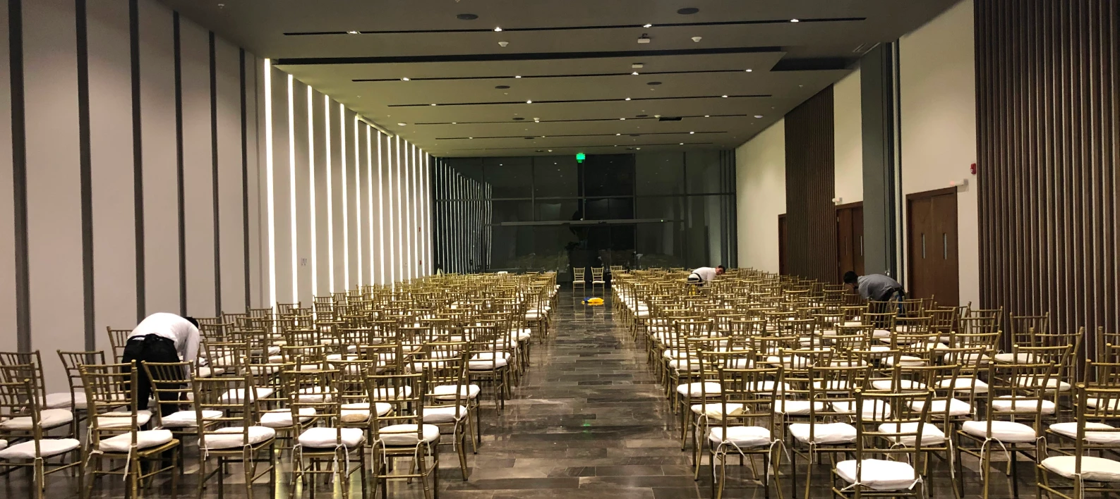 Pasillo de sala con filas de sillas doradas y mesas, ambiente de evento.
