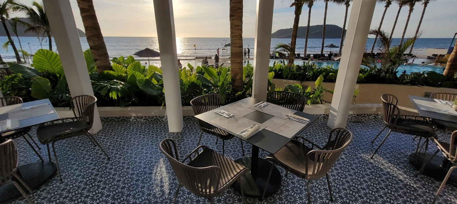 Terraza con mesa y sillas, palmeras y vista al mar al atardecer