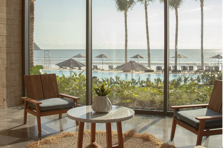 Terraza con dos sillones, mesa de madera y vista al mar con palmeras