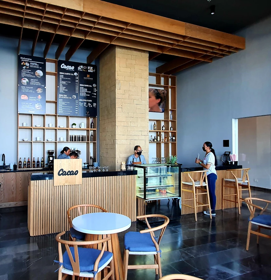 Interior de cafeter&iacute;a con barra, vitrinas y mesas, personal atendiendo.