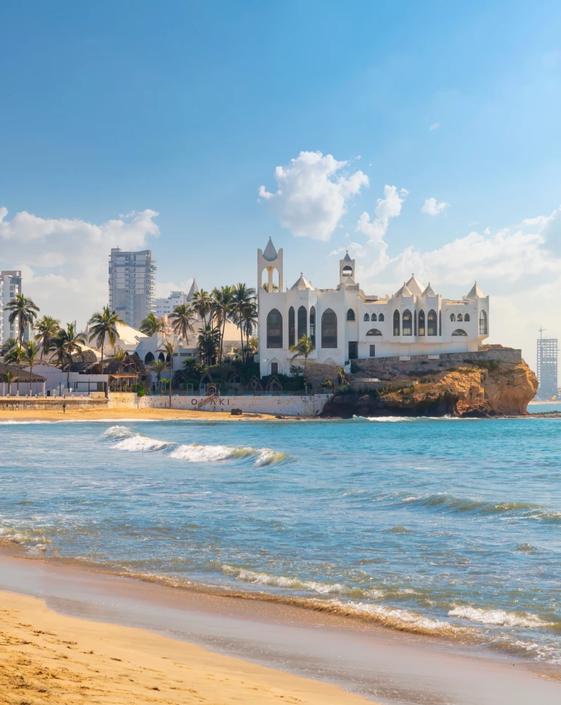 Playa tropical con iglesia blanca junto al acantilado y palmeras, al atardecer