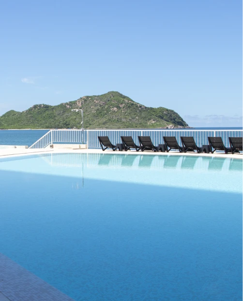 Piscina azul con tumbonas y vista a una colina verde bajo el cielo azul