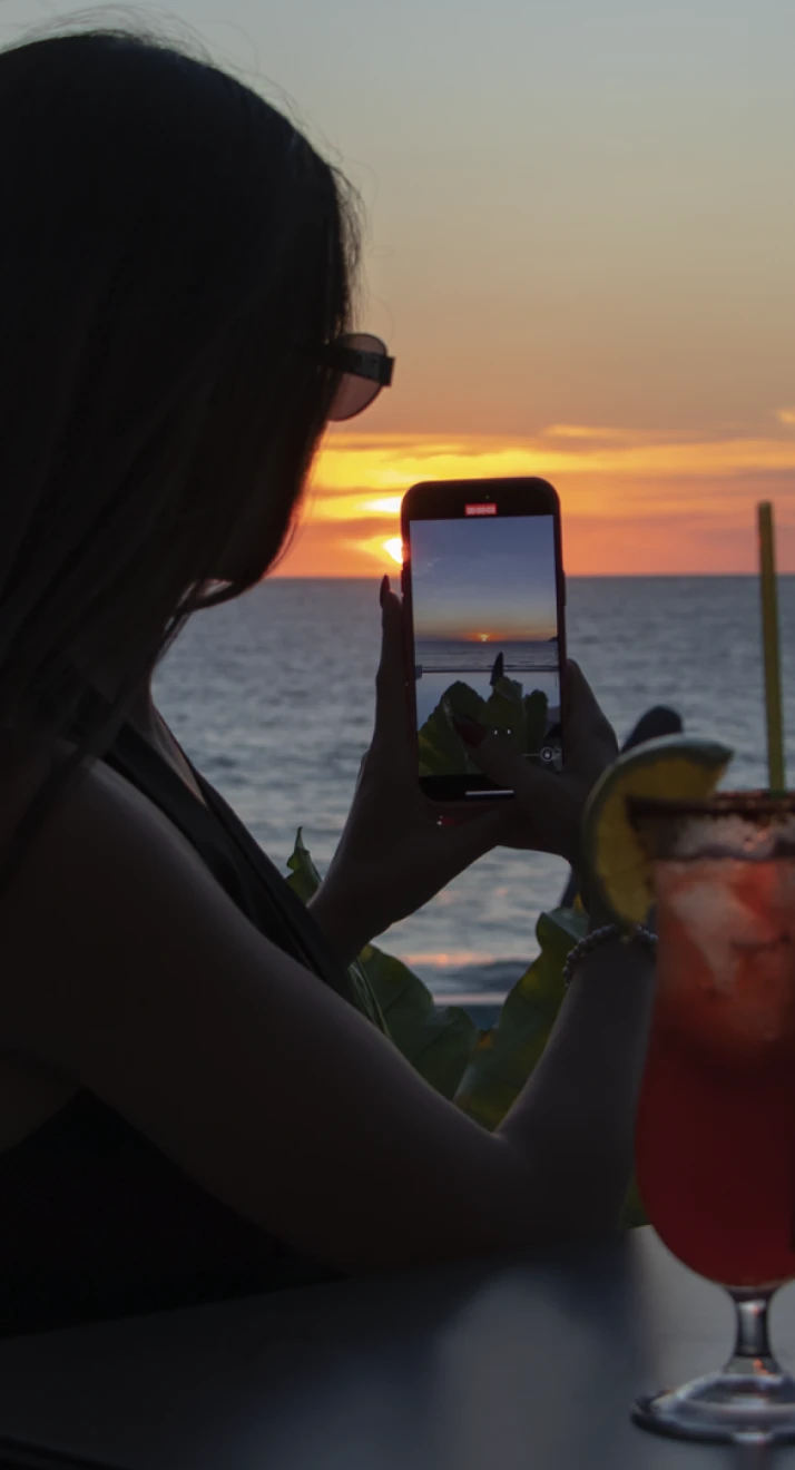 Mujer en primer plano toma una foto del atardecer en el mar con el m&oacute;vil