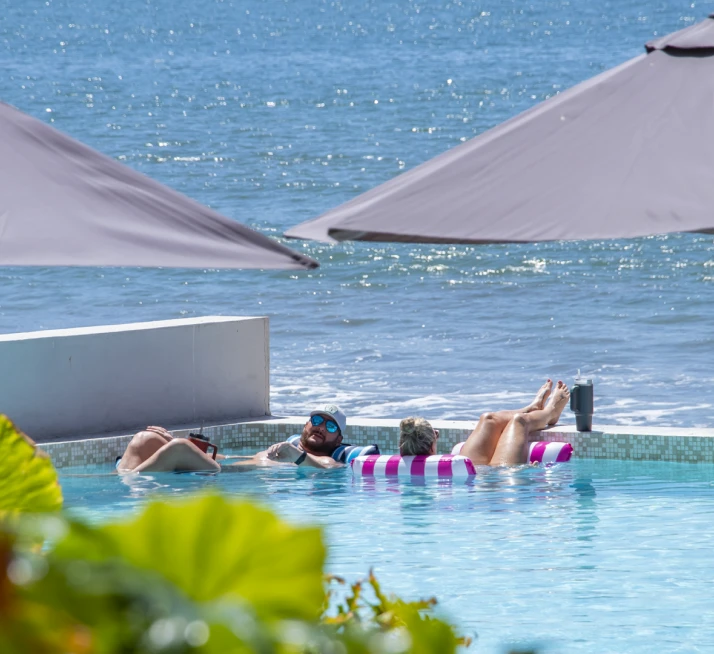 Hombres relaj&aacute;ndose en una piscina bajo sombrillas y al lado del mar