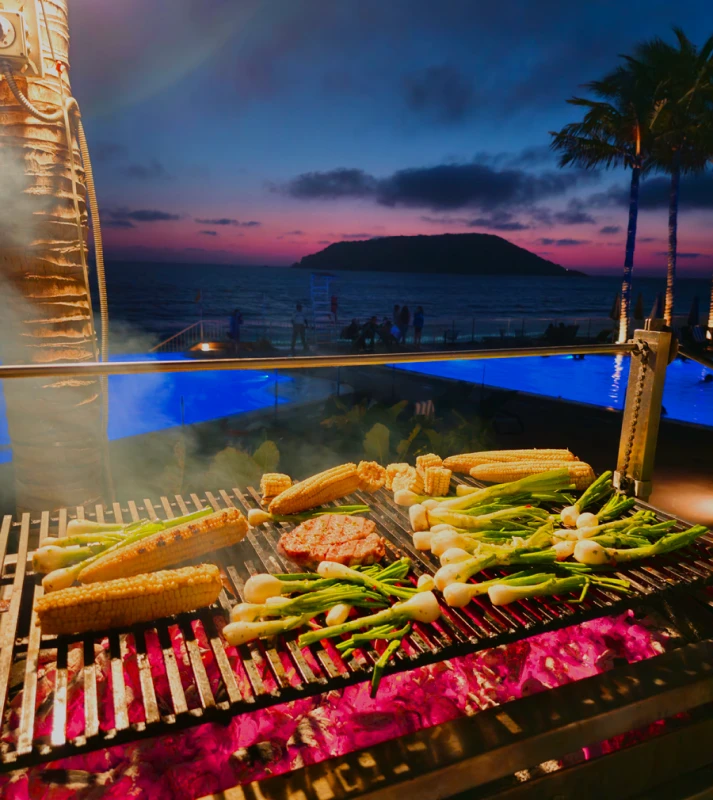 Parrilla con ma&iacute;z y vegetales as&aacute;ndose frente al mar al atardecer