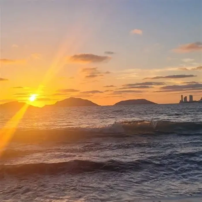 Atardecer sobre el mar con olas y el sol saliendo detr&aacute;s de monta&ntilde;as