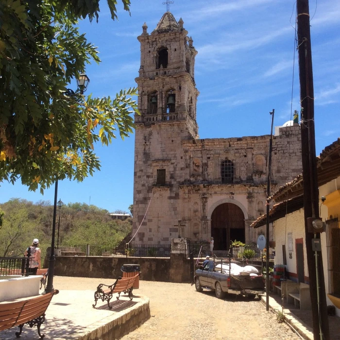 Torre de iglesia hist&oacute;rica con patio y bancos bajo el cielo azul