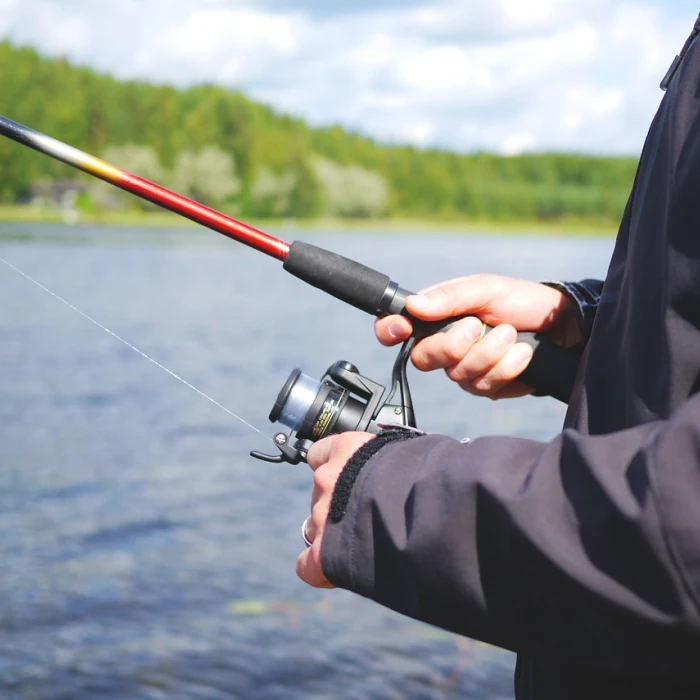 Persona pescando con ca&ntilde;a y carrete en un lago, junto a vegetaci&oacute;n.