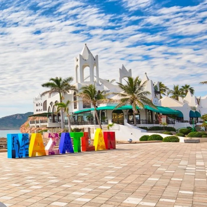 Hotel blanco con palmeras, sombrillas azules y mural de letras de colores