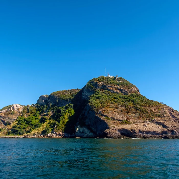 Isla rocosa con vegetaci&oacute;n y faro en la cima, frente al mar azul