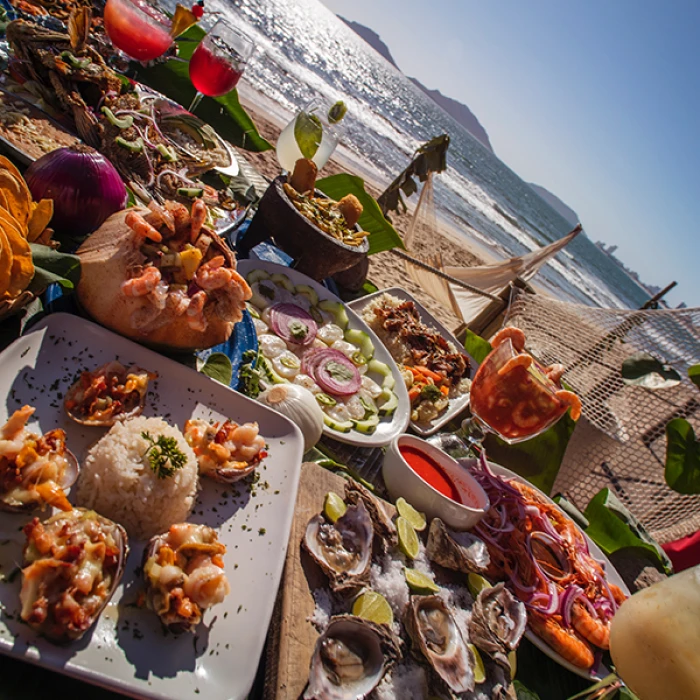Mesa con mariscos y ceviches, limones y redes al fondo en la playa