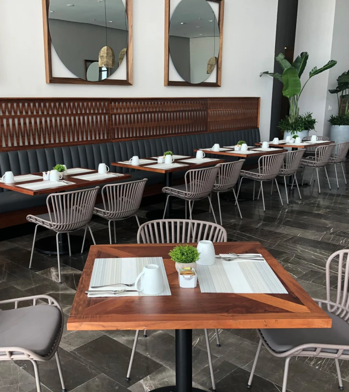 Comedor al aire libre con mesas de madera, sillas grises y decoraci&oacute;n verde