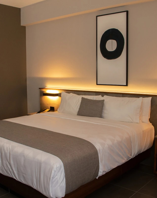Habitaci&oacute;n de hotel moderna con cama doble y l&aacute;mpara, pared iluminada.