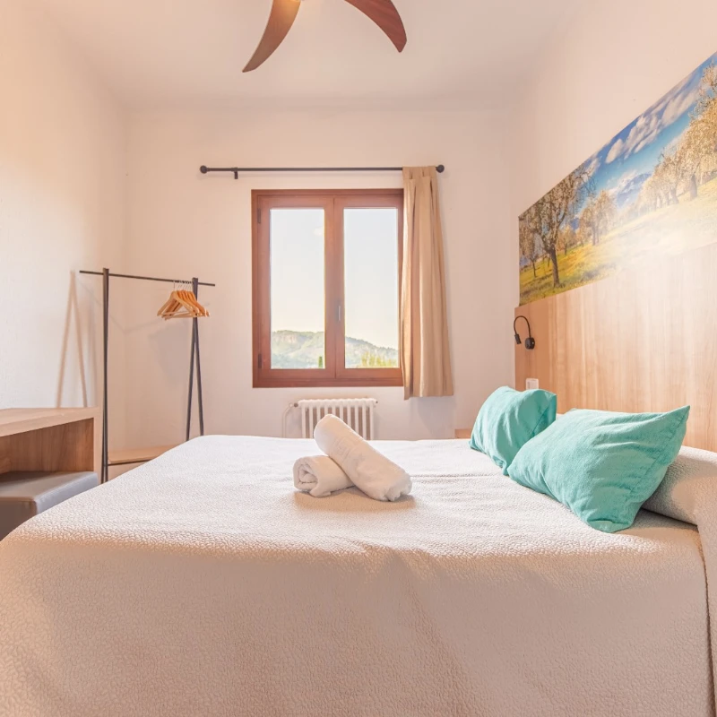 Dormitorio luminoso con cama, cojines azules y ventana con cortinas beige