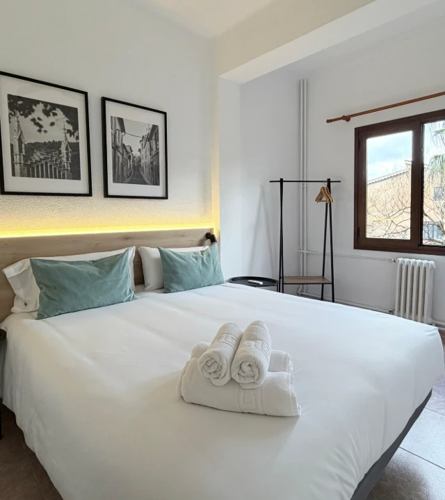 Dormitorio moderno con cama blanca, cojines azules y ropa doblada.
