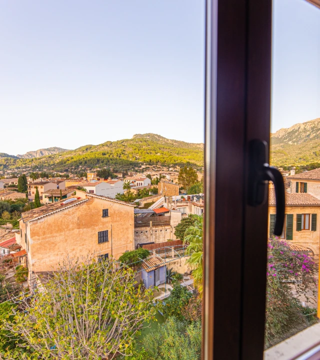 Vista de casas mediterr&aacute;neas y colinas a trav&eacute;s de una ventana abierta