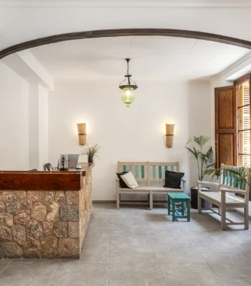 Recepción con mostrador de piedra, banca y sillones en un vestíbulo.
