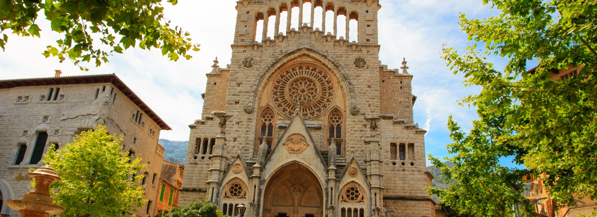 Fachada de una iglesia de piedra con rosetón y árboles verdes alrededor